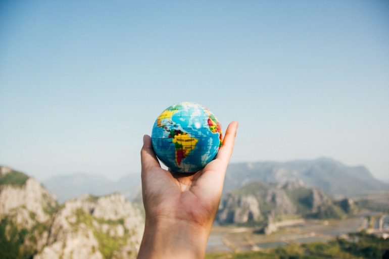 Hand hält die Welt mit blauem Himmel im Hintergrund